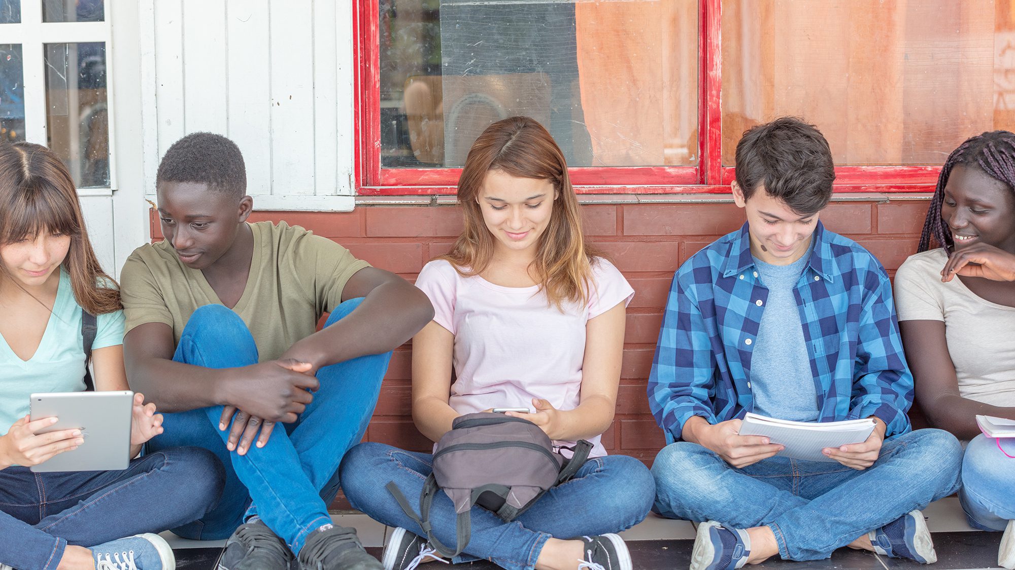 Multi ethnic group of teenagers using electronics and reading bo