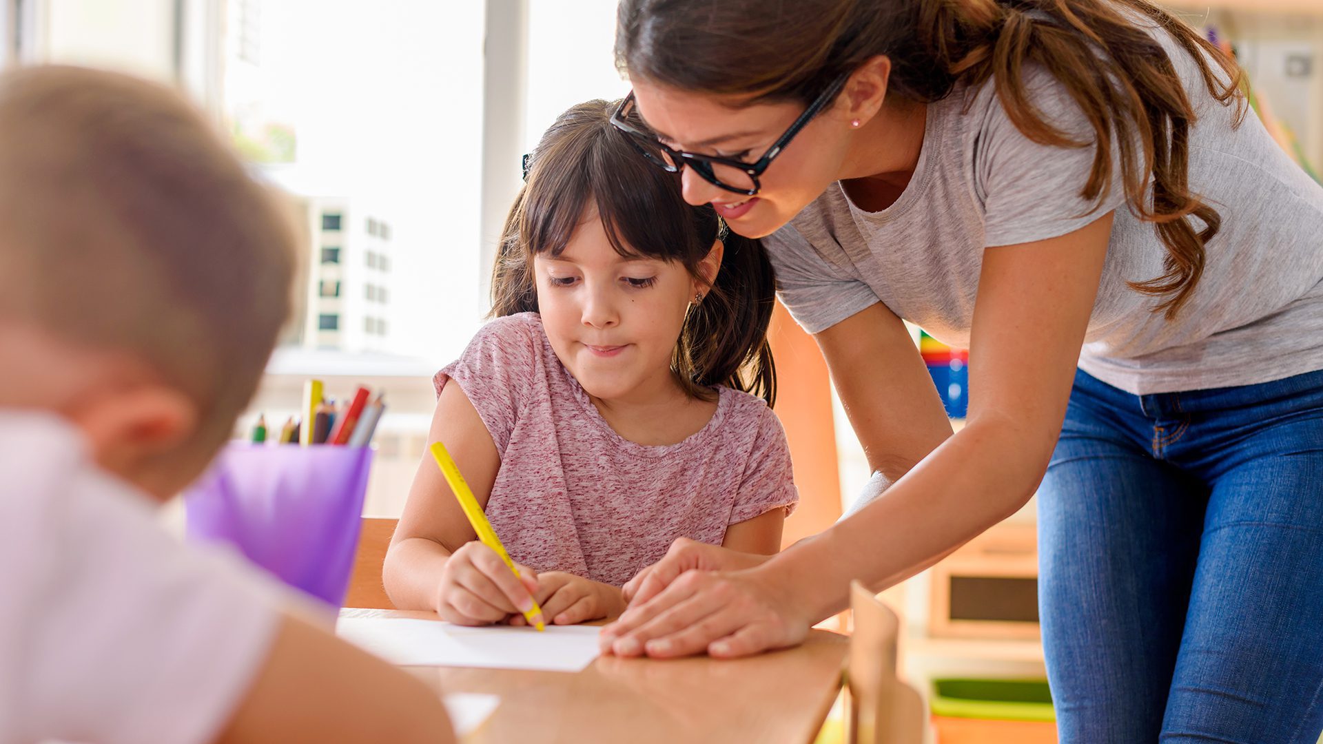 Preschool teacher assisting children with their drawings.