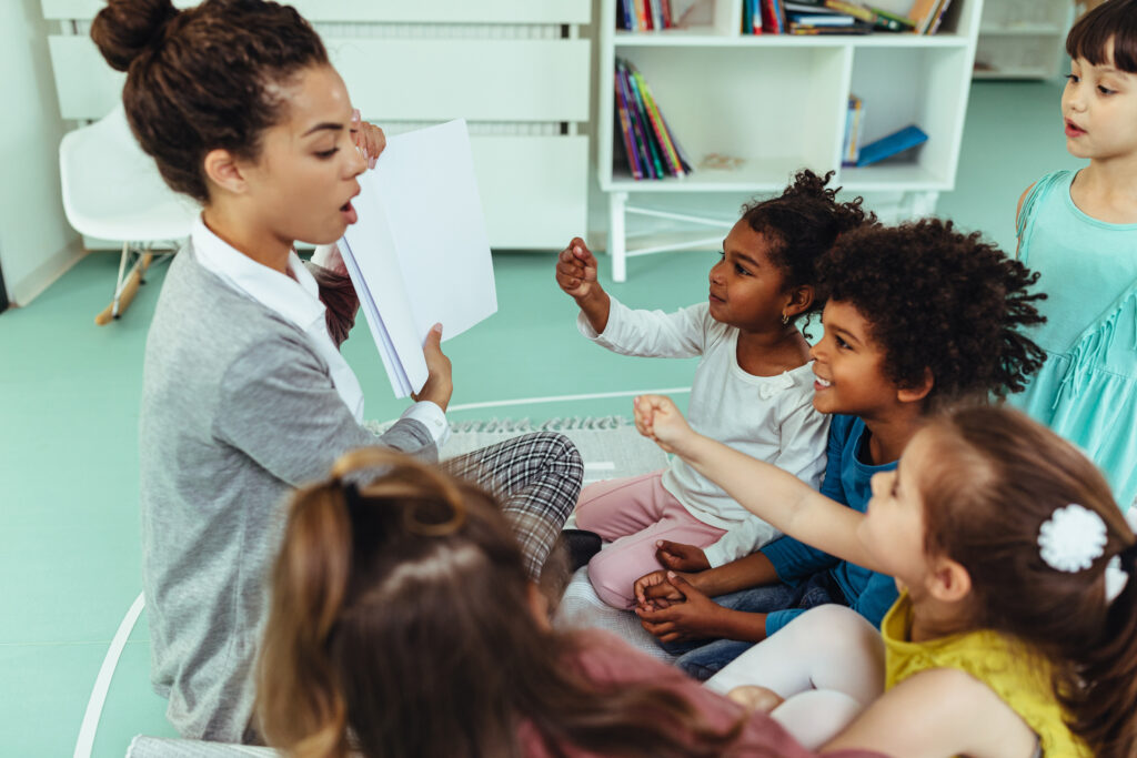 Female teacher reading a story to cute children at kindergarten