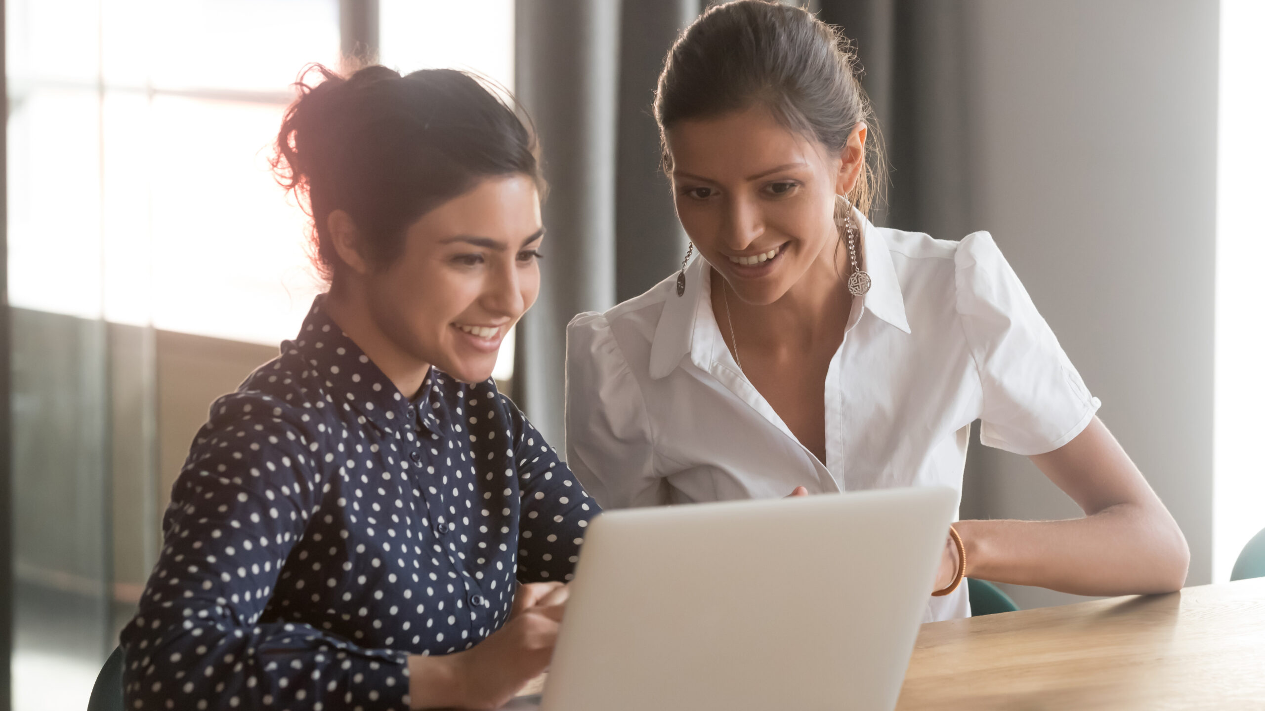 Two women work together on a laptop.